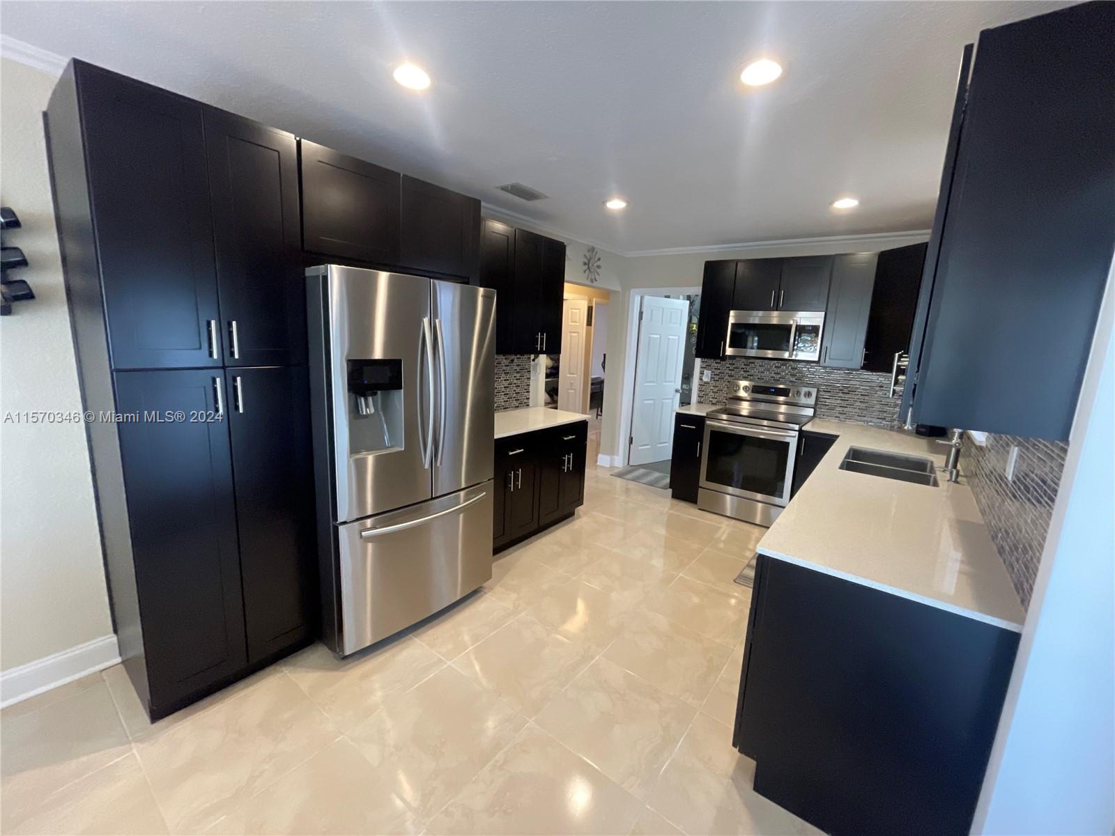 Immerse yourself in culinary luxury with this fully remodeled kitchen, boasting ample counters, deep pantry with soft-touch closure, on the drawers and a complete stainless steel Samsung package. Dark cabinetry contrasts elegantly with light polished countertops, creating a visually stunning space. Tiled floors lead to the dual stainless steel sink, combining functionality with sophistication. Experience seamless flow throughout the home, inviting you to indulge in refined living.